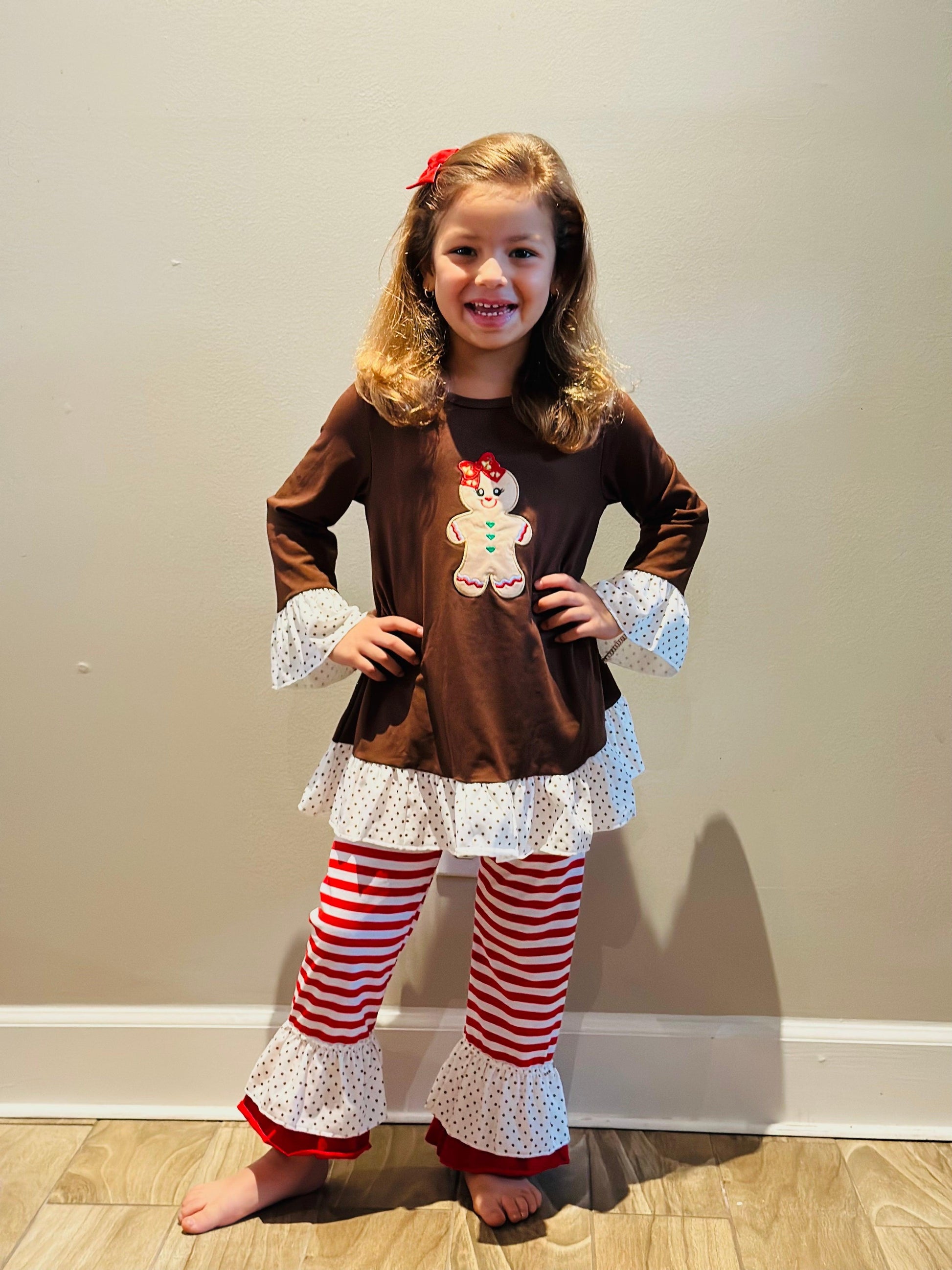 Your little girl will be looking festive and stylish in the Girls Holiday Gingerbread Outfit. This outfit features an adorable red and white striped gingerbread-themed top with ruffles and long sleeves. Perfect for Christmas!